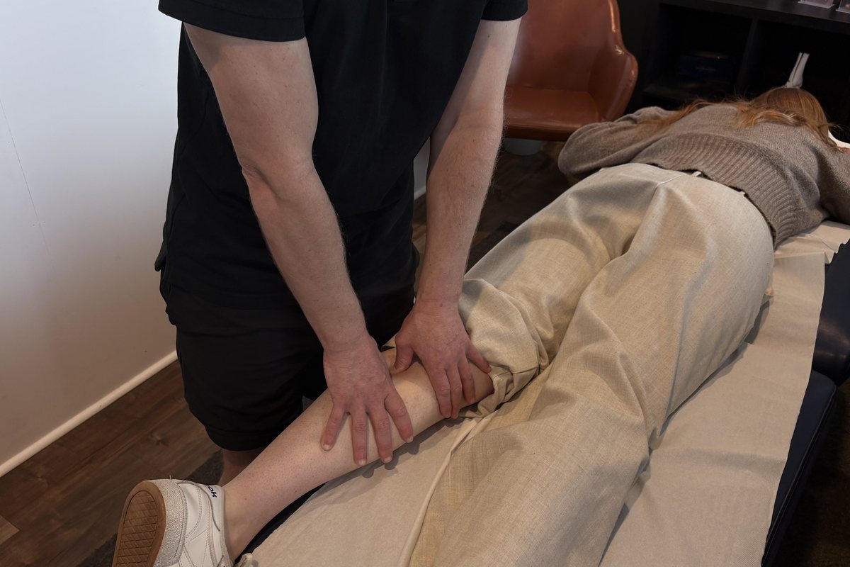 Dale Peirson working a client's calf through clothing while they lie on the treatment table
