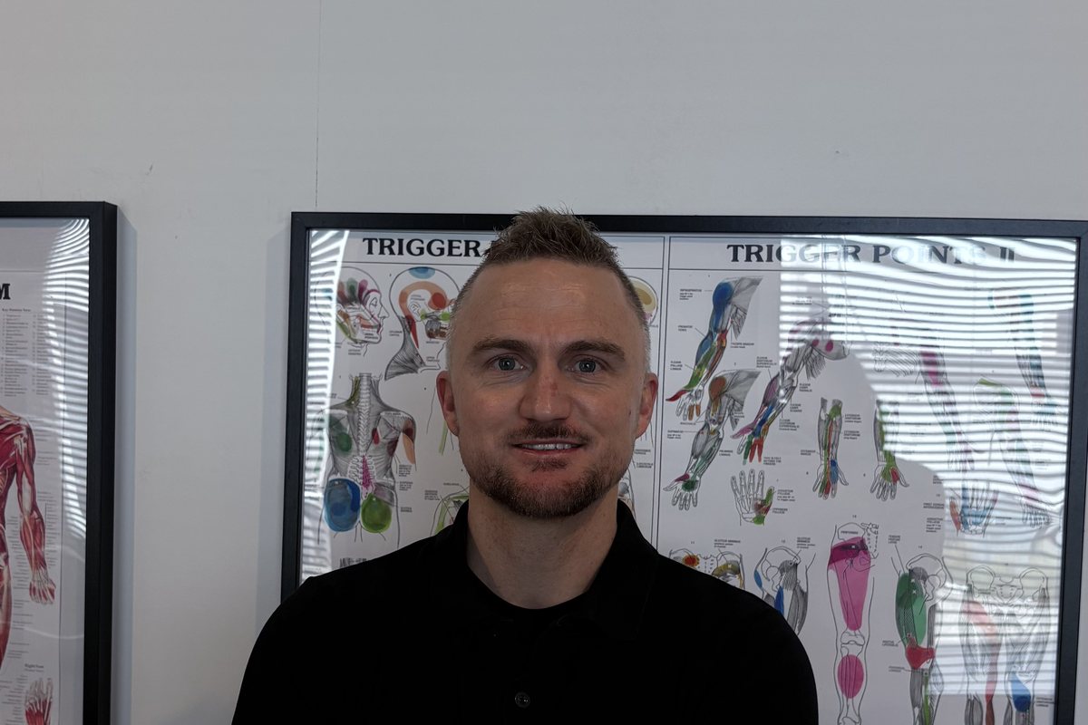 Dale Peirson, Senior Myotherapist, standing with his arms crossed in front of trigger point charts
