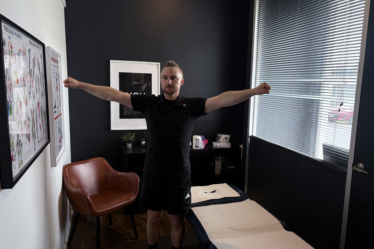 Dale Peirson standing with both arms out wide at shoulder height in the treatment room