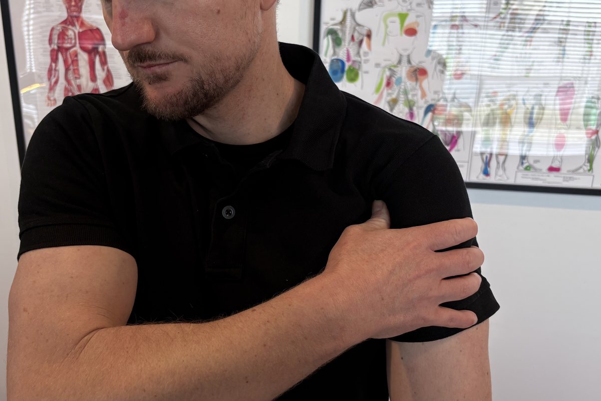 Dale Peirson gripping the front of his own shoulder to show where shoulder pain is usually felt