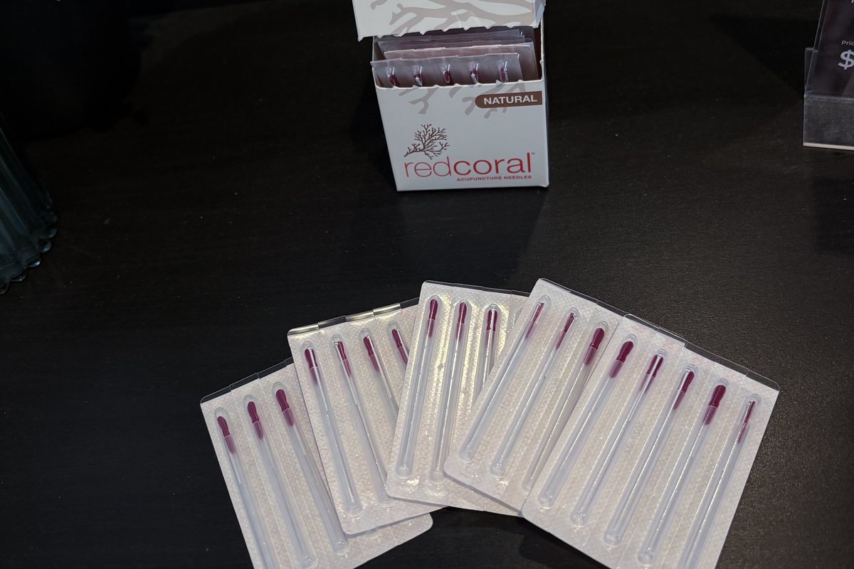 Sealed single-use dry needling needles fanned out beside their box on the bench