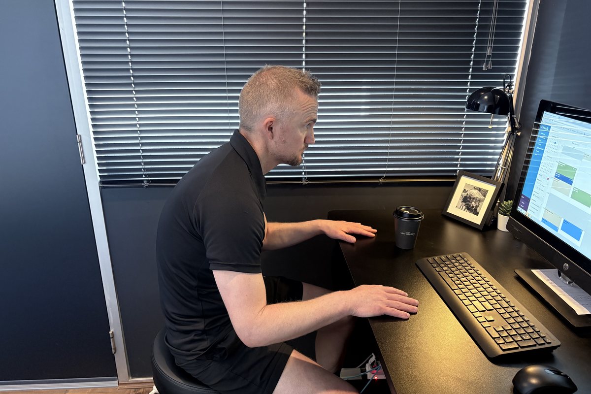 Dale Peirson sitting upright at the same desk with his ribs stacked over his hips